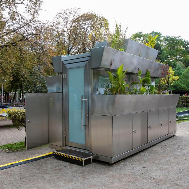 Ein modernes, begrüntes Toilettenhäuschen steht in einem Park.