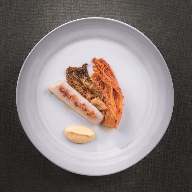 Ein Teller mit Kimchi, einer Wurst und einer gelben Soße.