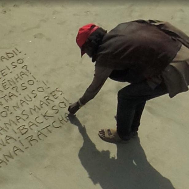 Ein Mann mit roter Kappe schreibt Wörter in einer unbekannten Sprache in den Sand.