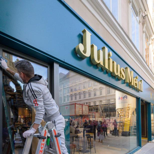 Ein Fensterputzer reinigt das Schaufenster von Julius Meinl.