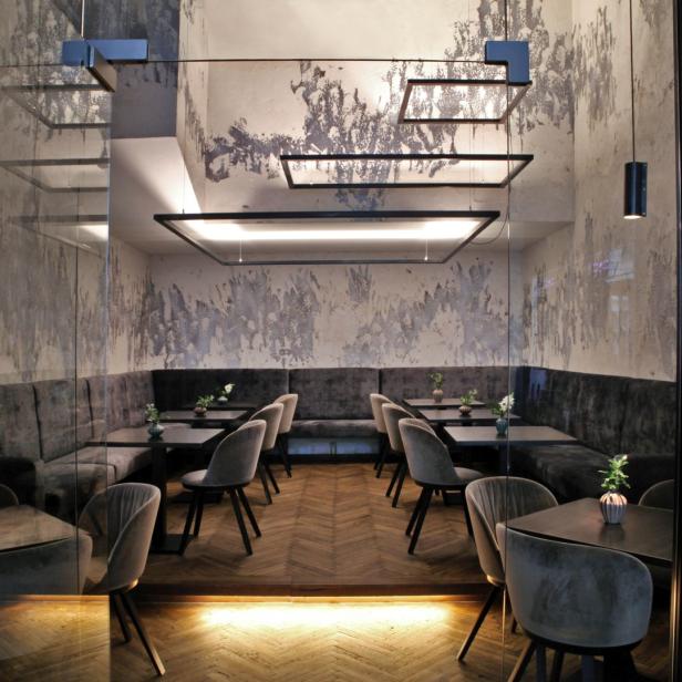 Ein elegantes Restaurant mit grauen Samtstühlen und dunklen Holztischen.
