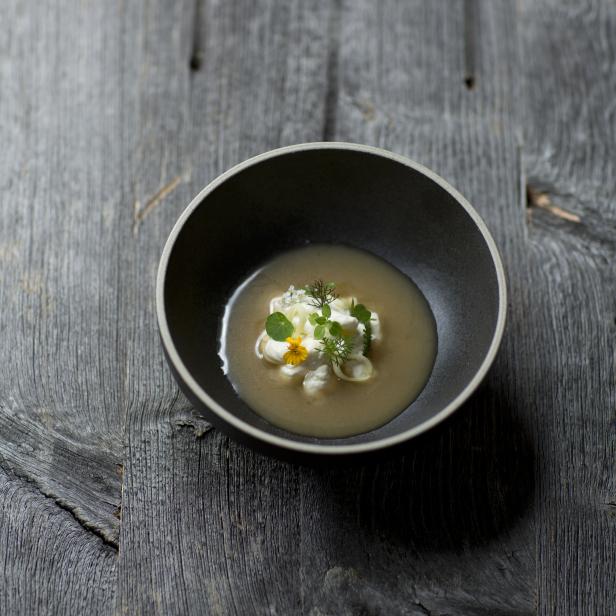 Eine Schüssel Suppe mit Kräutern und Blüten auf einem Holztisch.