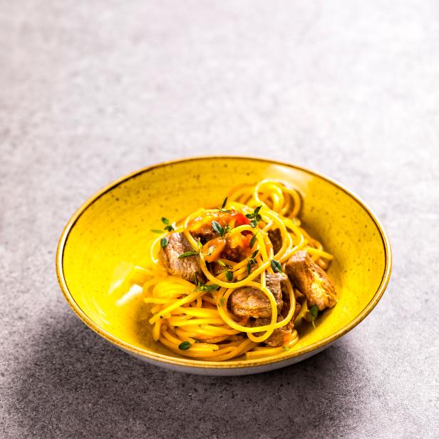 Spaghetti mit Fleischstücken und Kräutern in einer gelben Schüssel.
