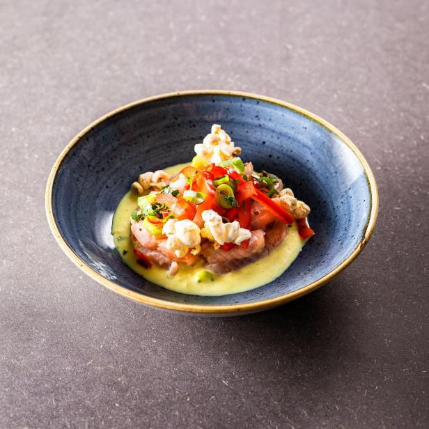 Ein Teller mit Ceviche, garniert mit Popcorn und roten Paprikastreifen.