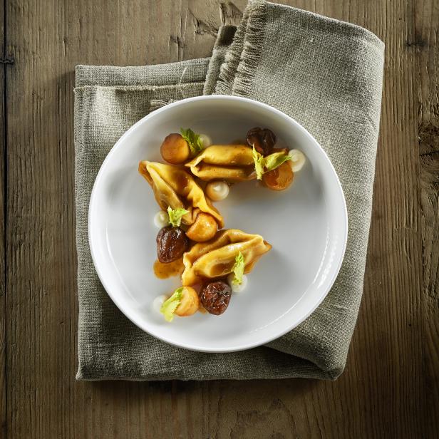 Ein Teller Tortelloni mit Maronen und Salbei auf einem Holztisch.