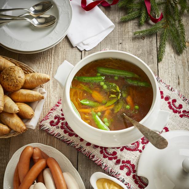 Ein festliches Mahl mit Suppe, Würstchen, Brot und Käse auf einem Holztisch.