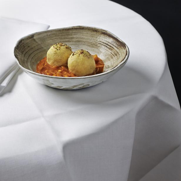 Zwei Kartoffelknödel liegen in einer Schale mit Tomatensauce auf einem weißen Tisch.