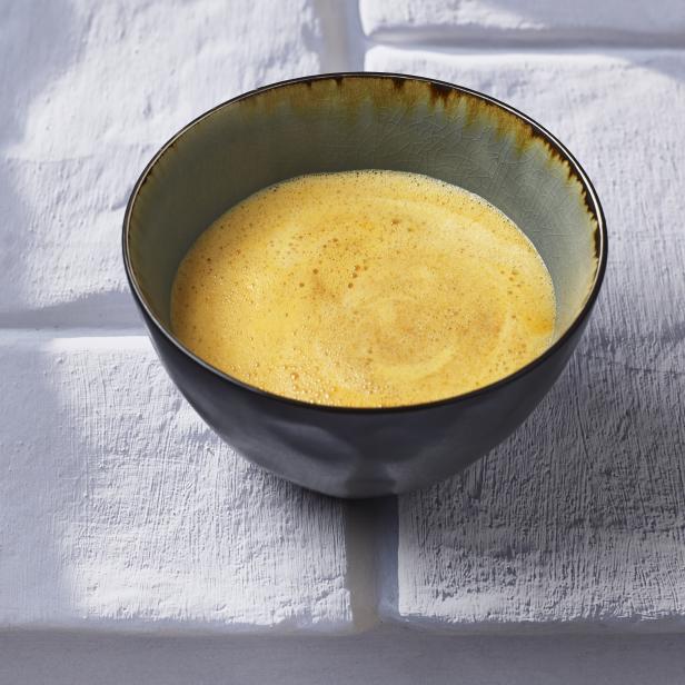 Eine Schüssel mit gelber Suppe steht auf einem weißen Tisch.