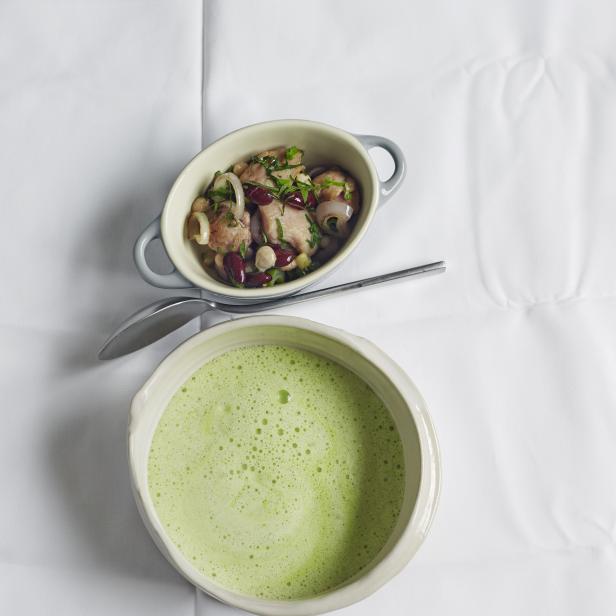 Eine Schüssel grüne Suppe und eine Schale mit Bohnen und Fleisch auf einem weißen Tuch.