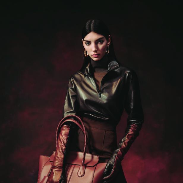 Eine Frau in brauner Lederjacke und Hose hält eine passende Handtasche.