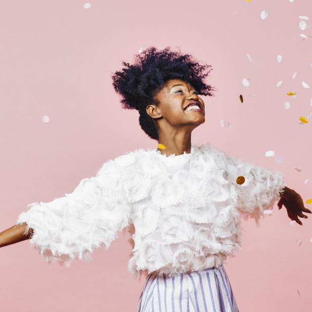 Eine Frau mit Afro-Haar feiert mit Konfetti vor einem rosa Hintergrund.
