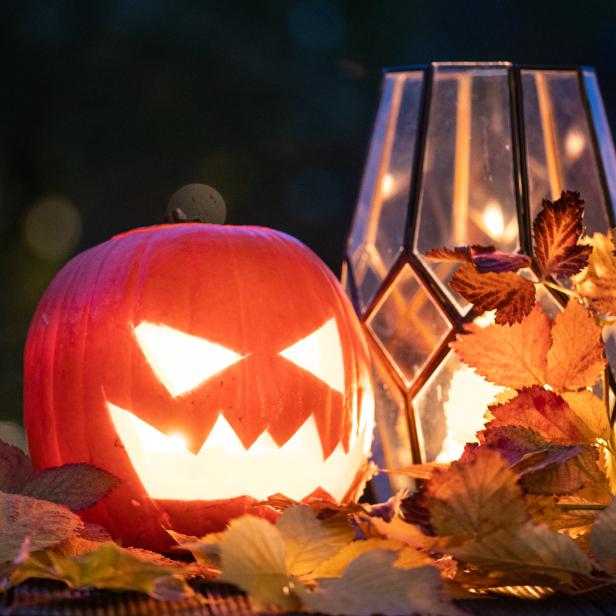 Ein geschnitzter Halloween-Kürbis leuchtet neben einer Laterne und Herbstlaub.
