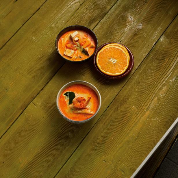 Zwei Schalen mit Tom Yum Suppe und eine halbe Orange auf einem Holztisch.