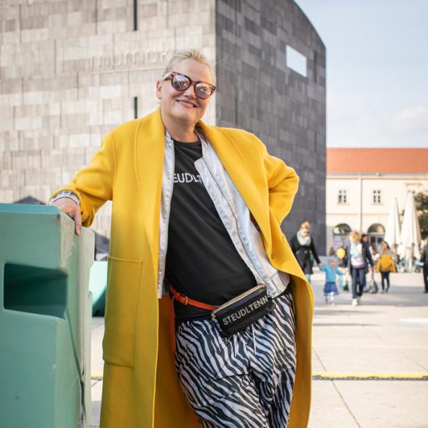 Eine Frau mit gelbem Mantel und Zebrahose posiert vor dem mumok in Wien.