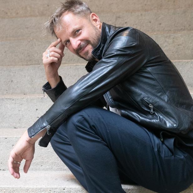 Ein Mann mit Lederjacke sitzt auf einer Steintreppe.