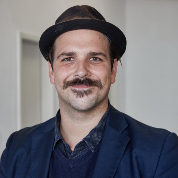 Ein Mann mit Hut und Schnurrbart blickt in die Kamera.