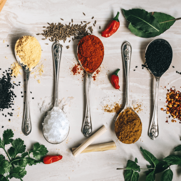 Verschiedene Gewürze, Kräuter und Chilis sind dekorativ auf einem hellen Untergrund angeordnet.