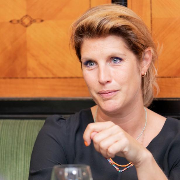 Eine Frau mit blonden Haaren und blauem Eyeliner sitzt an einem Tisch.