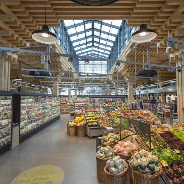 Ein gut sortierter Supermarkt mit Obst, Gemüse und Kühlregalen unter einem Glasdach.