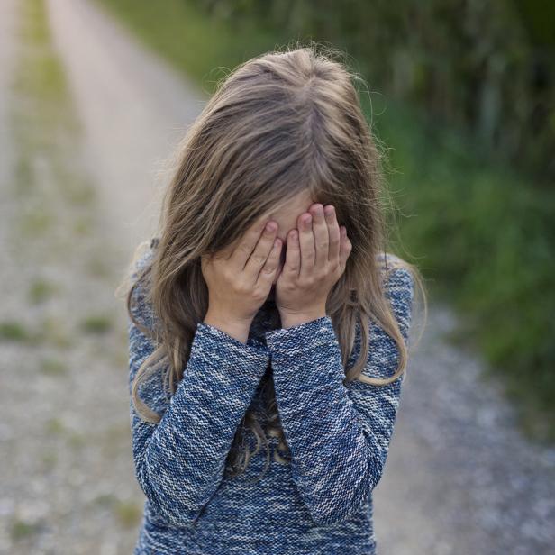 Ein Mädchen mit blonden Haaren hält die Hände vor ihr Gesicht.