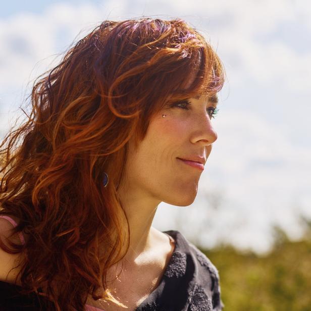 Eine Frau mit roten Haaren und einem Piercing im Gesicht schaut zur Seite.