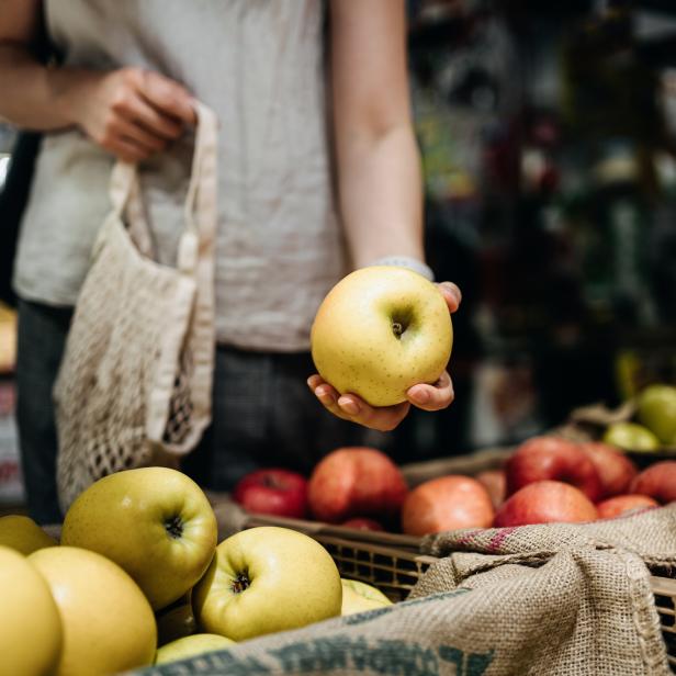 Eine Frau hält einen gelben Apfel auf einem Markt in der Hand.