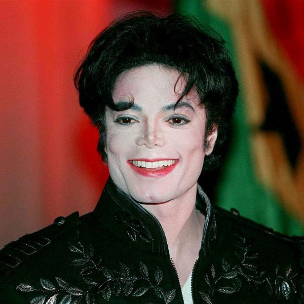 Michael Jackson lächelt in einer schwarzen Jacke mit silbernen Verzierungen.