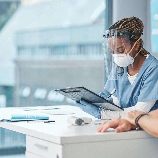 Eine Ärztin mit Gesichtsschutz notiert Informationen von einem Patienten.