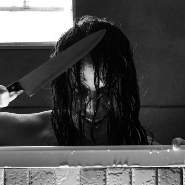 Eine Frau mit nassen Haaren hält ein Messer in der Badewanne.