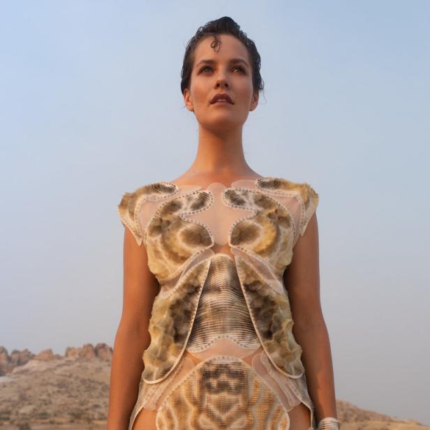 Eine Frau in einem futuristischen Kleid steht in einer trockenen Landschaft.