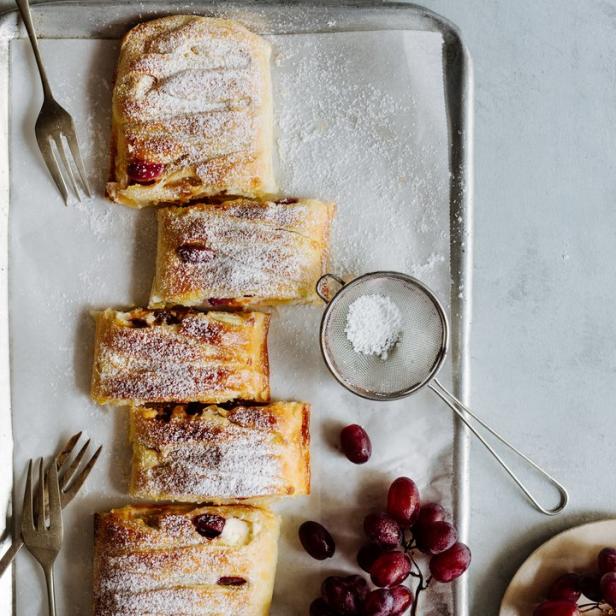 Ein aufgeschnittener Strudel mit Puderzucker und roten Trauben auf einem Backblech.