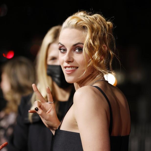 Kristen Stewart auf dem roten Teppich, die Zunge leicht herausgestreckt und ein Friedenszeichen zeigend.