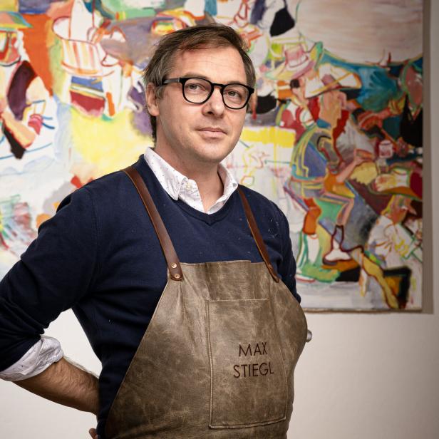 Max Stiegl, ein Künstler, steht vor einem seiner farbenfrohen Gemälde.