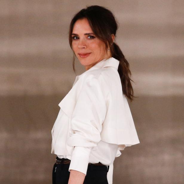 Victoria Beckham posiert in einer weißen Bluse und schwarzen Hose.