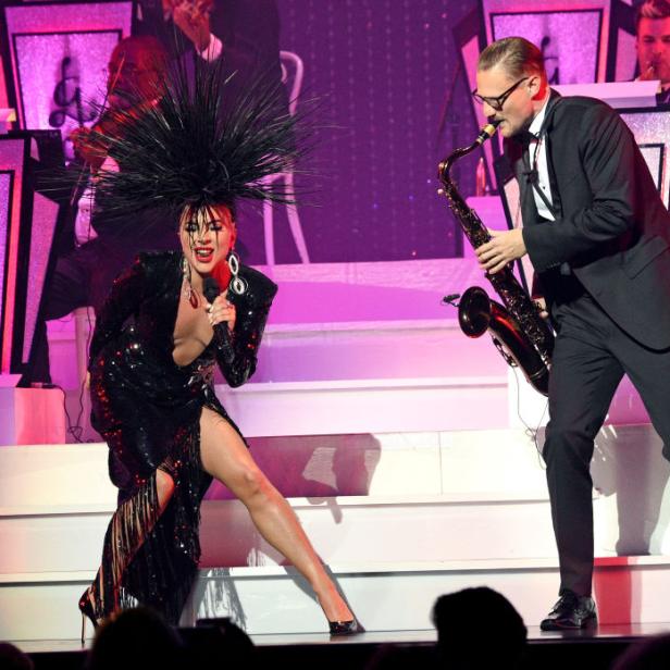 Lady Gaga tritt mit einem Saxophonisten und einem Orchester auf einer Bühne auf.