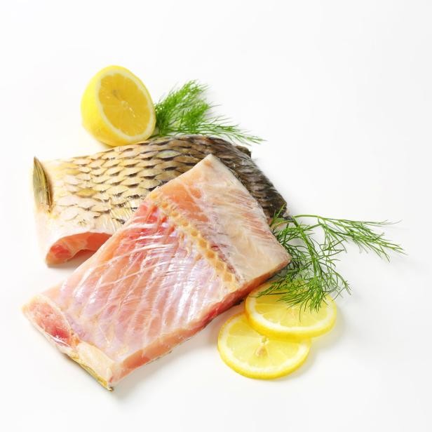 Zwei rohe Karpfenfilets mit Zitrone und Dill auf weißem Grund.