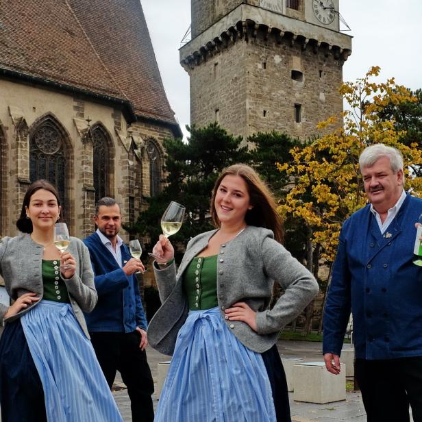 Personen in Tracht posieren mit Wein vor dem Hintergrund von Perchtoldsdorf.