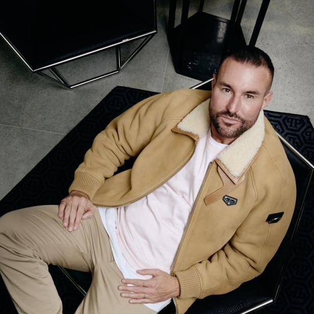 Ein Mann mit Bart sitzt in einem Sessel und trägt eine Jacke mit Fellkragen.