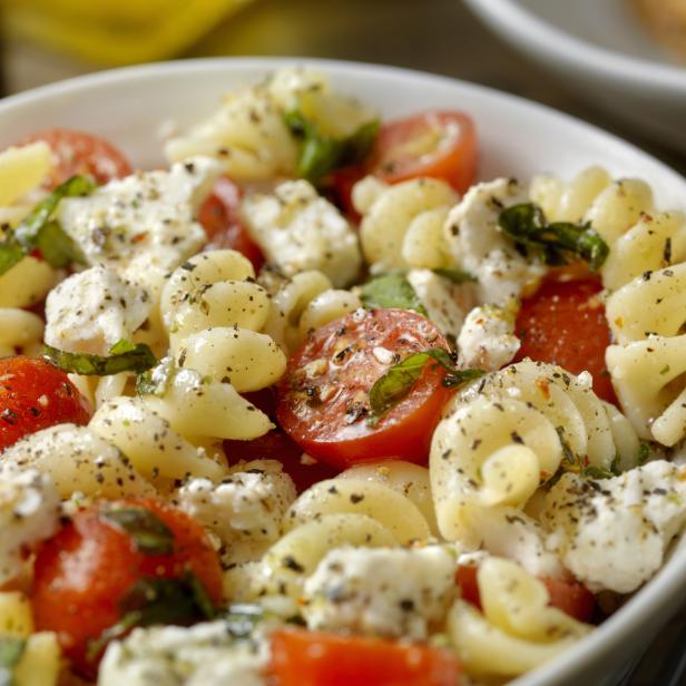 Ein Teller mit Nudelsalat, Tomaten, Mozzarella und Basilikum.