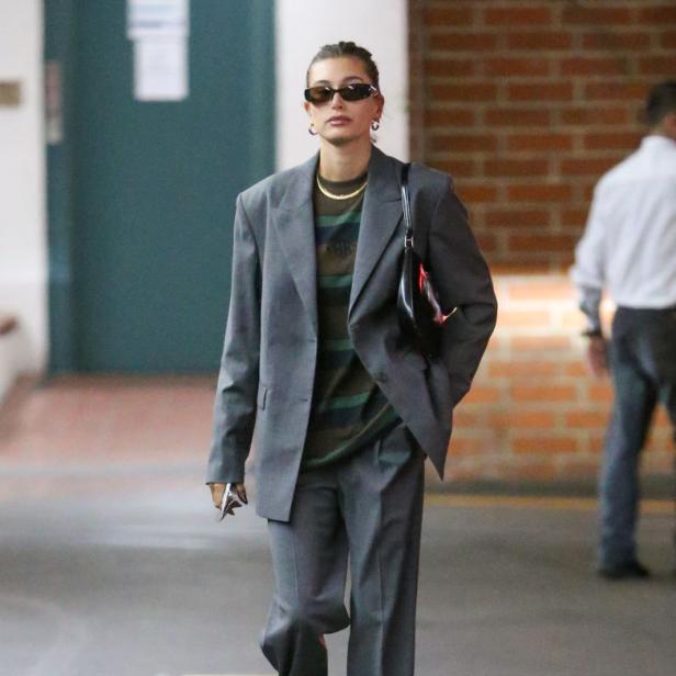 Hailey Bieber trägt einen übergroßen grauen Hosenanzug und weiße Turnschuhe.