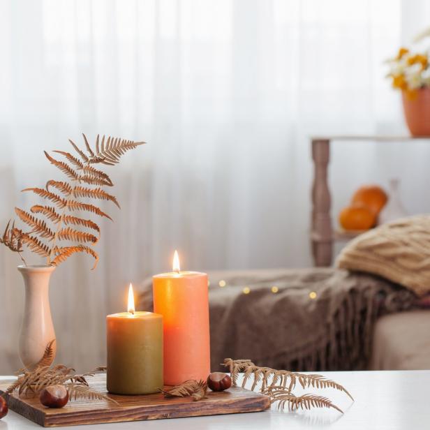 Zwei brennende Kerzen und Herbstdekorationen auf einem Tisch.