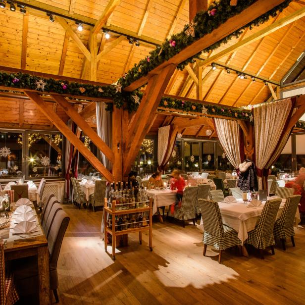 Ein festlich geschmücktes Restaurant mit Holzbalkendecke und gedeckten Tischen.