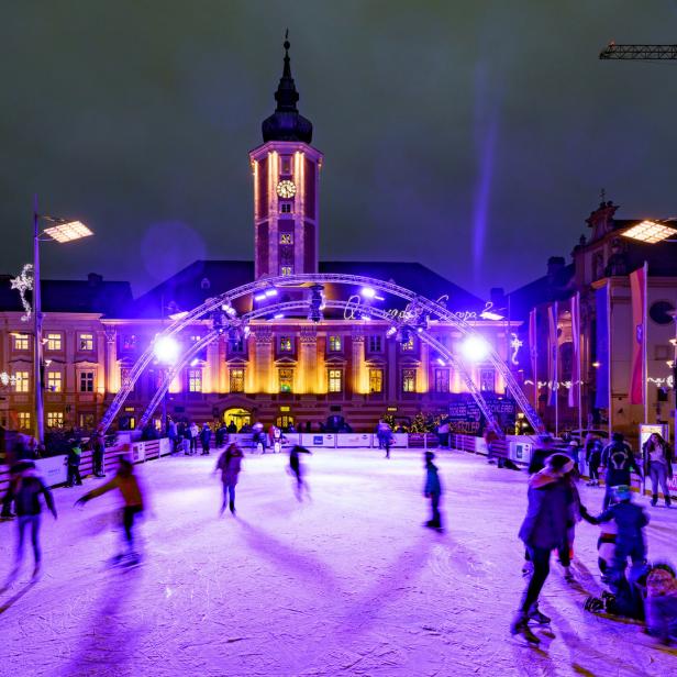 Schlittschuhläufer auf einer Eisbahn vor dem Rathaus von Wels bei Nacht.