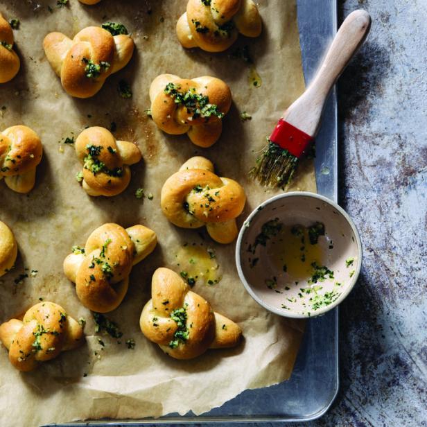 Eine Reihe von Knoblauchknoten auf einem Backblech mit einer Schüssel und einem Pinsel.