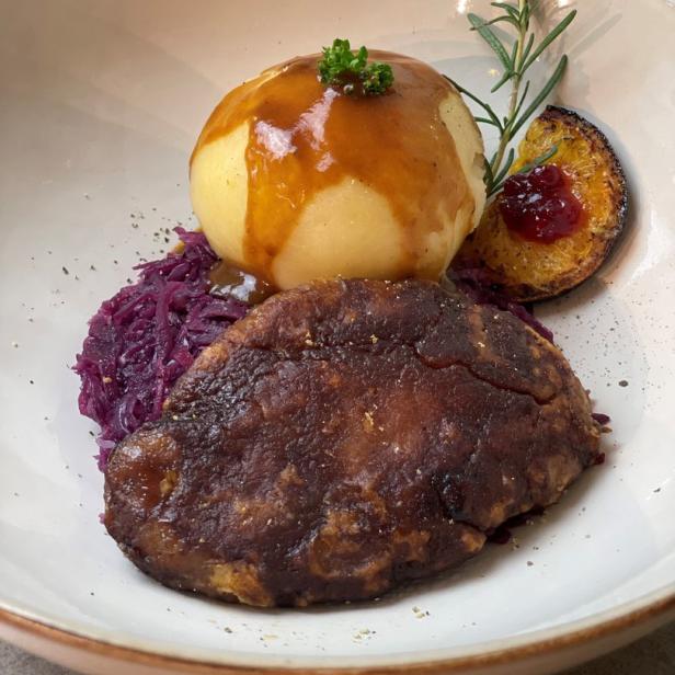 Ein Teller mit Seitanbraten, Rotkohl, Kartoffelknödel und Pflaume mit Soße.