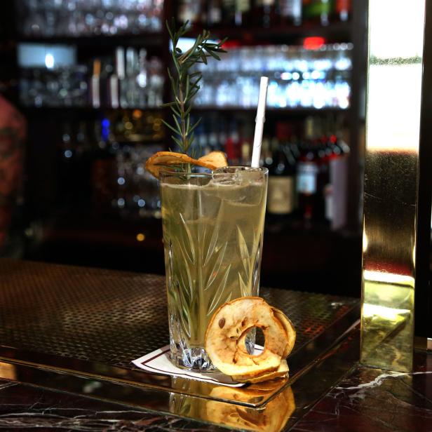 Ein Cocktail mit Apfelchips und Rosmarin auf einer Bar.