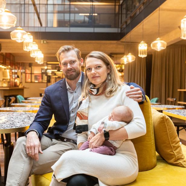 Eine Familie mit einem Neugeborenen sitzt in einem modern eingerichteten Raum.