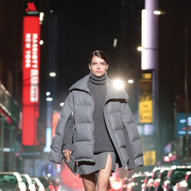 Eine Frau in einem grauen Outfit läuft nachts auf einer Straße in New York.