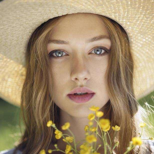 Eine junge Frau mit Strohhut hält einen Strauß gelber Blumen.