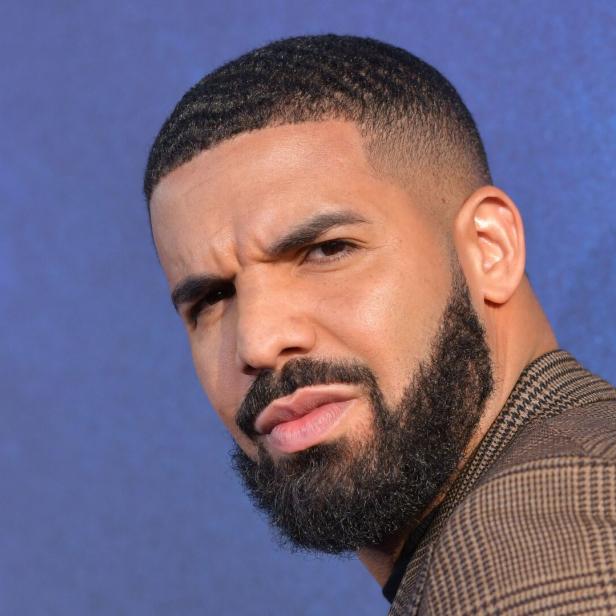 Porträt des kanadischen Rappers Drake mit Bart und kariertem Sakko vor blauem Hintergrund.